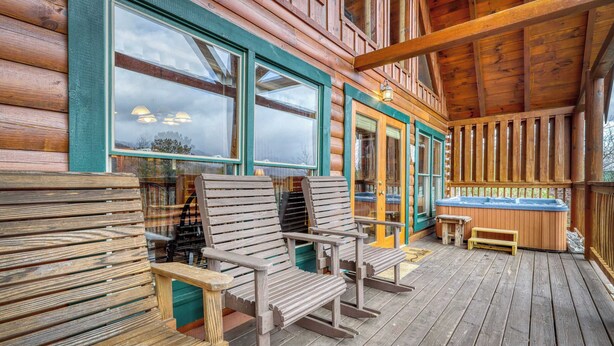 Eine Holzhütte mit Veranda, zwei Schaukelstühlen, einem Whirlpool und Blick auf die umliegende Landschaft.