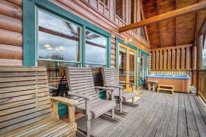 Een houten chalet met een veranda, twee schommelstoelen, een jacuzzi en uitzicht op het omliggende landschap.