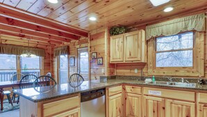 Eine Holzhütte mit einer Küche, einer Granit-Arbeitsplatte, Holzschränken, einem Geschirrspüler und einem großen Fenster.