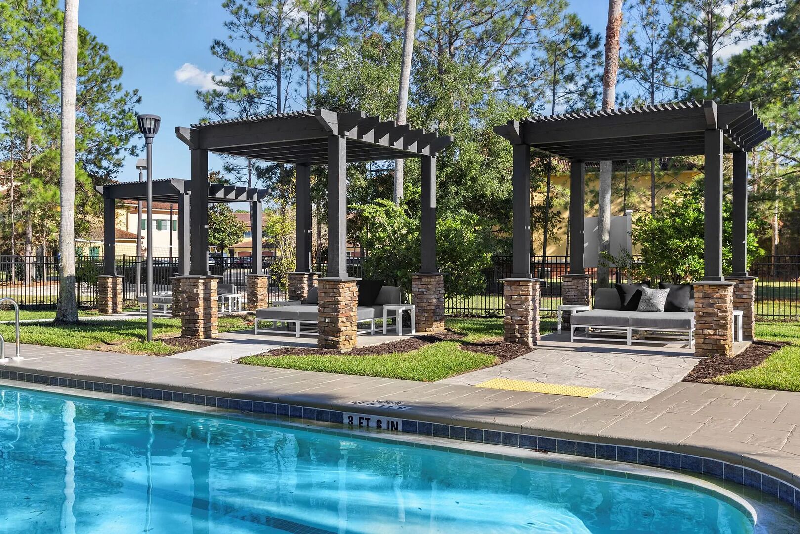 A pool area with two outdoor seating areas, stone pillars, and a clear blue pool.