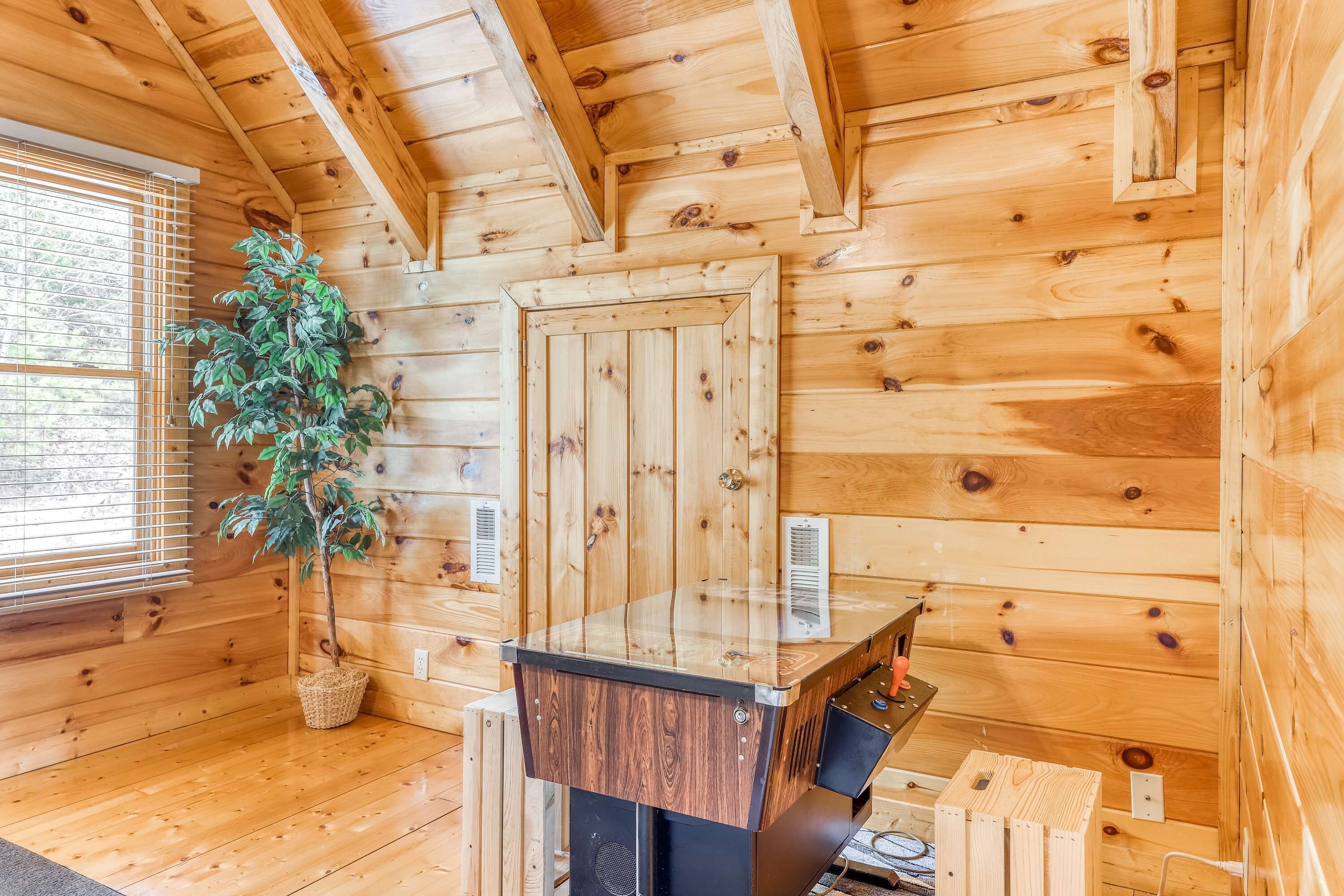 Ein Interieur einer Holzhütte mit einem Holztisch, einer Topfpflanze und einem Fenster mit Jalousien.