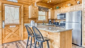 Cocina de cabaña de madera con una isla central, taburetes de bar, un refrigerador de acero inoxidable y una ventana con persianas.