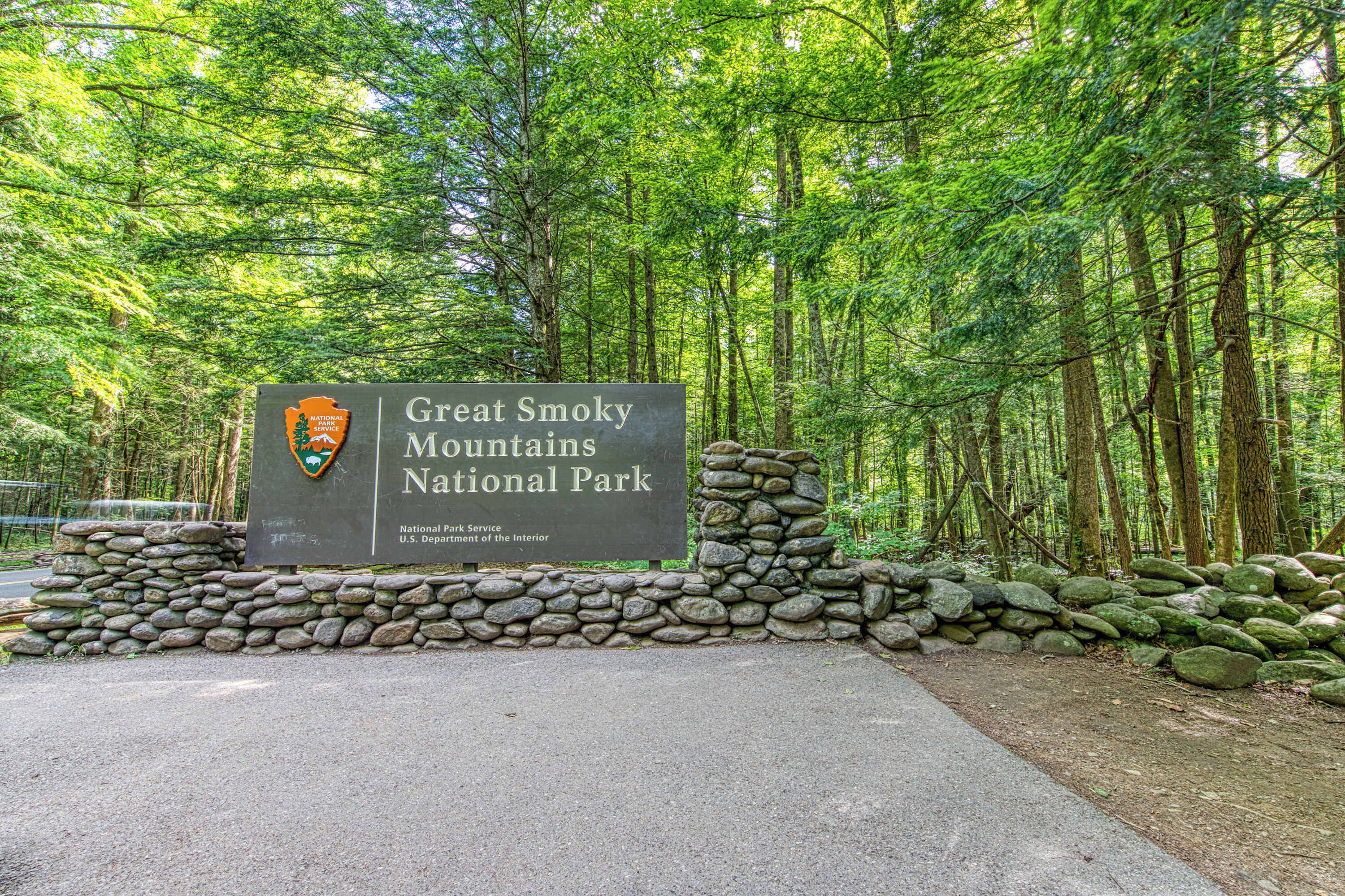 A sign for Great Smoky Mountains National Park with a stone wall and forested background.