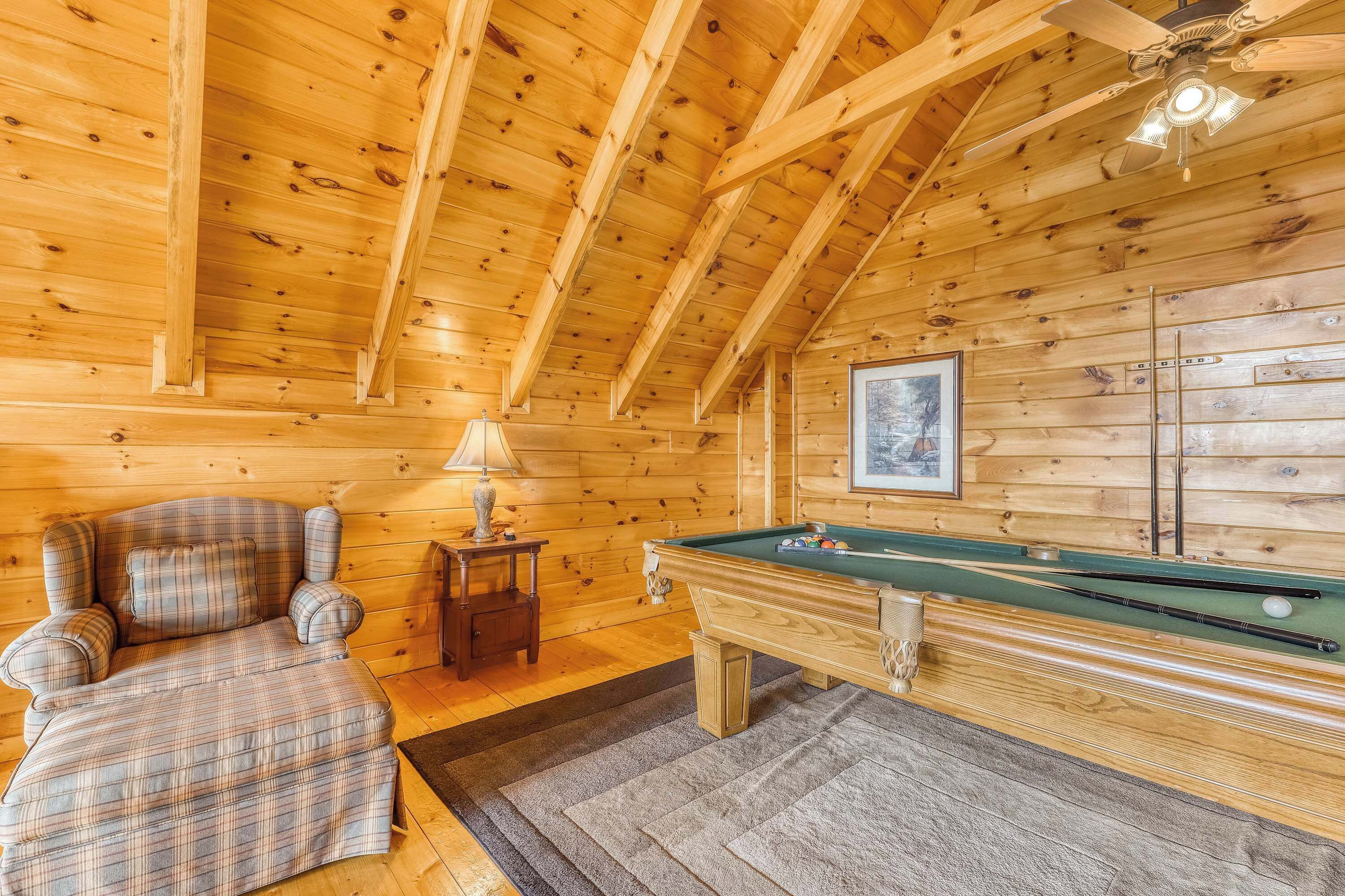 Ein Holzblockhaus mit Pooltisch, kariertem Sofa und Deckenventilator.
