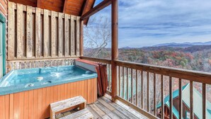 Una terraza de madera con un jacuzzi y zona de estar, con vistas a un paisaje montañoso.