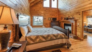 Ein Schlafzimmer in einer Blockhütte mit einem Bett, einem Nachttisch, einer Lampe, einem Kamin und einem Deckenventilator.