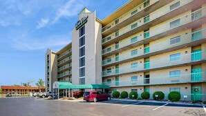 Un hotel a più piani con un cartello ben visibile, un parcheggio e un tendone verde sull'ingresso.