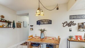 Zona pranzo con tavolo in legno, sedie e lampadario a sospensione. Decorazioni a parete, tra cui un cartello con la scritta “The Best Place To Be Is Together” e un altro con “ESPRESSO YOU Coffee”.