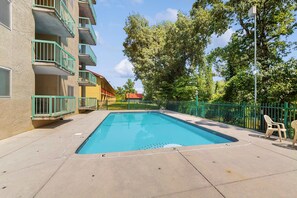 A swimming pool with a green fence, surrounded by a building with balconies and trees. - Cozy Fireplace, River Views, Walk to Downtown (Pigeon Forge)