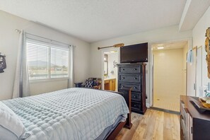 A bedroom with a bed, a dresser, a television, and a bathroom door. - Cozy Fireplace, River Views, Walk to Downtown (Pigeon Forge)