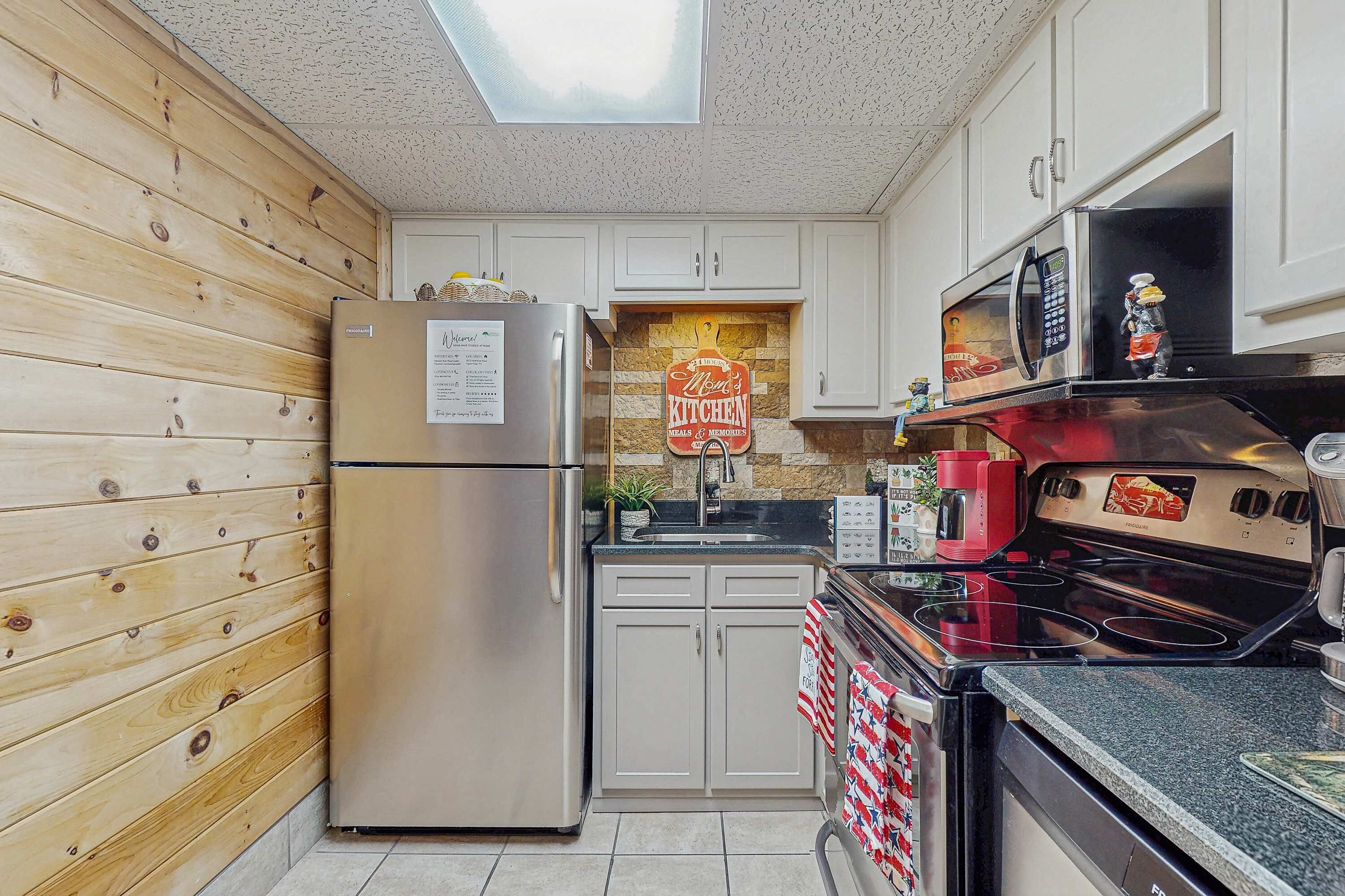 A compact kitchen with wooden paneling, a stainless steel refrigerator, a microwave, a gas stove, and a small sink.