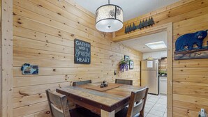 A wooden-paneled dining area with a table and chairs, a chandelier, and a bear decoration on the wall. - Charming Condo, River Views, Sleep 6, Fireplace, Pool (Pigeon Forge)