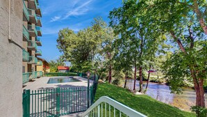 A courtyard with a swimming pool, a green fence, and a river. - Charming Condo, River Views, Sleep 6, Fireplace, Pool (Pigeon Forge)