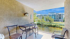 A balcony with a table and chairs, a view of a building across a water body, and a green railing. - Charming Condo, River Views, Sleep 6, Fireplace, Pool (Pigeon Forge)
