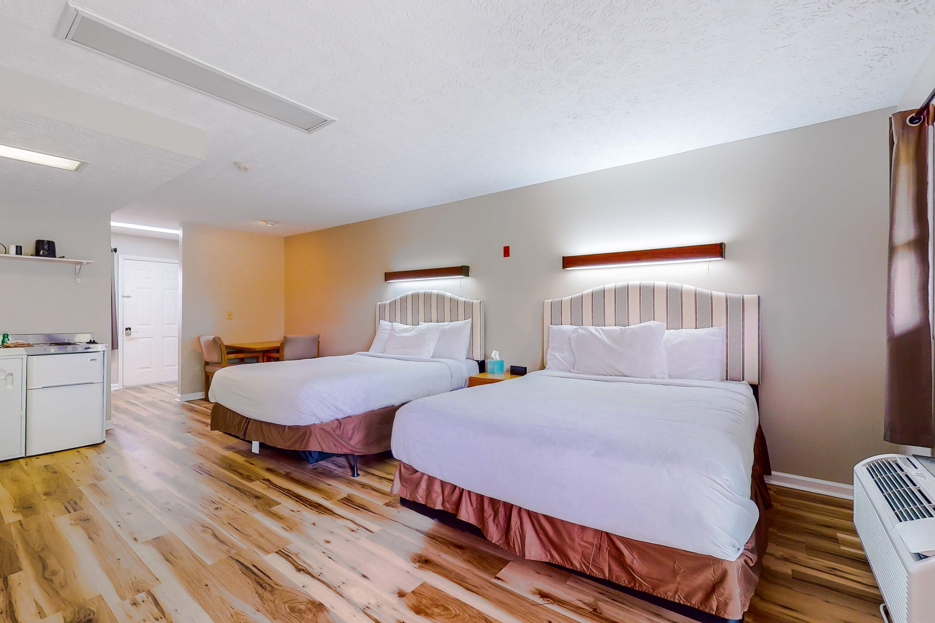 Quarto de hotel com duas camas, uma escrivaninha e uma cozinha compacta.