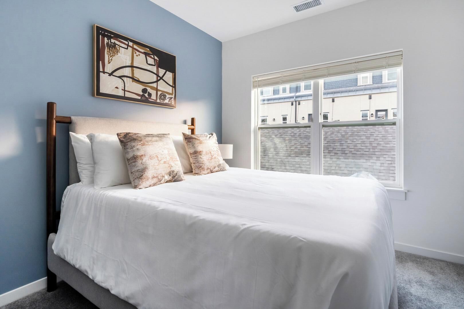 A bedroom with a bed, two pillows, a headboard, a window, and a painting on the wall.