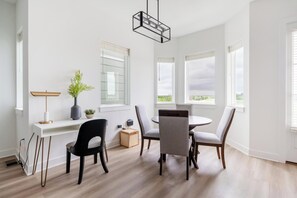 Un espace repas moderne avec une table blanche, quatre chaises, un vase avec une plante et un luminaire suspendu.