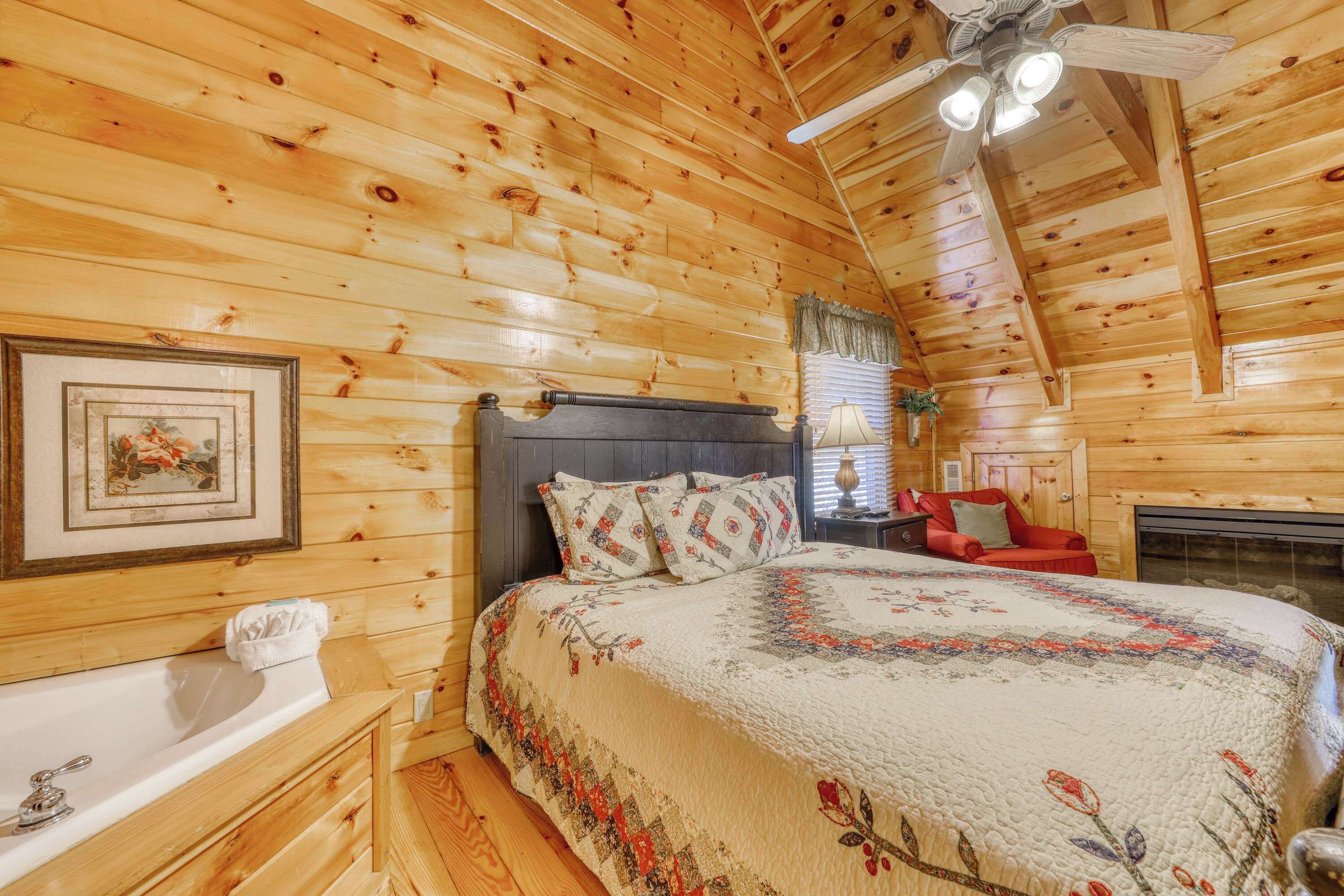 A cozy log cabin bedroom with a large bed, a wooden headboard, a ceiling fan, and a fireplace.