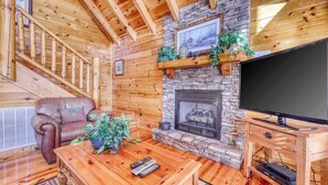 L’intérieur d’un chalet confortable, avec une cheminée en pierre, un meuble de rangement en bois, un canapé en cuir et un escalier.