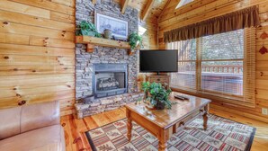 L’intérieur chaleureux d’un chalet avec des murs en bois, une cheminée en pierre, un téléviseur et un coin salon confortable.