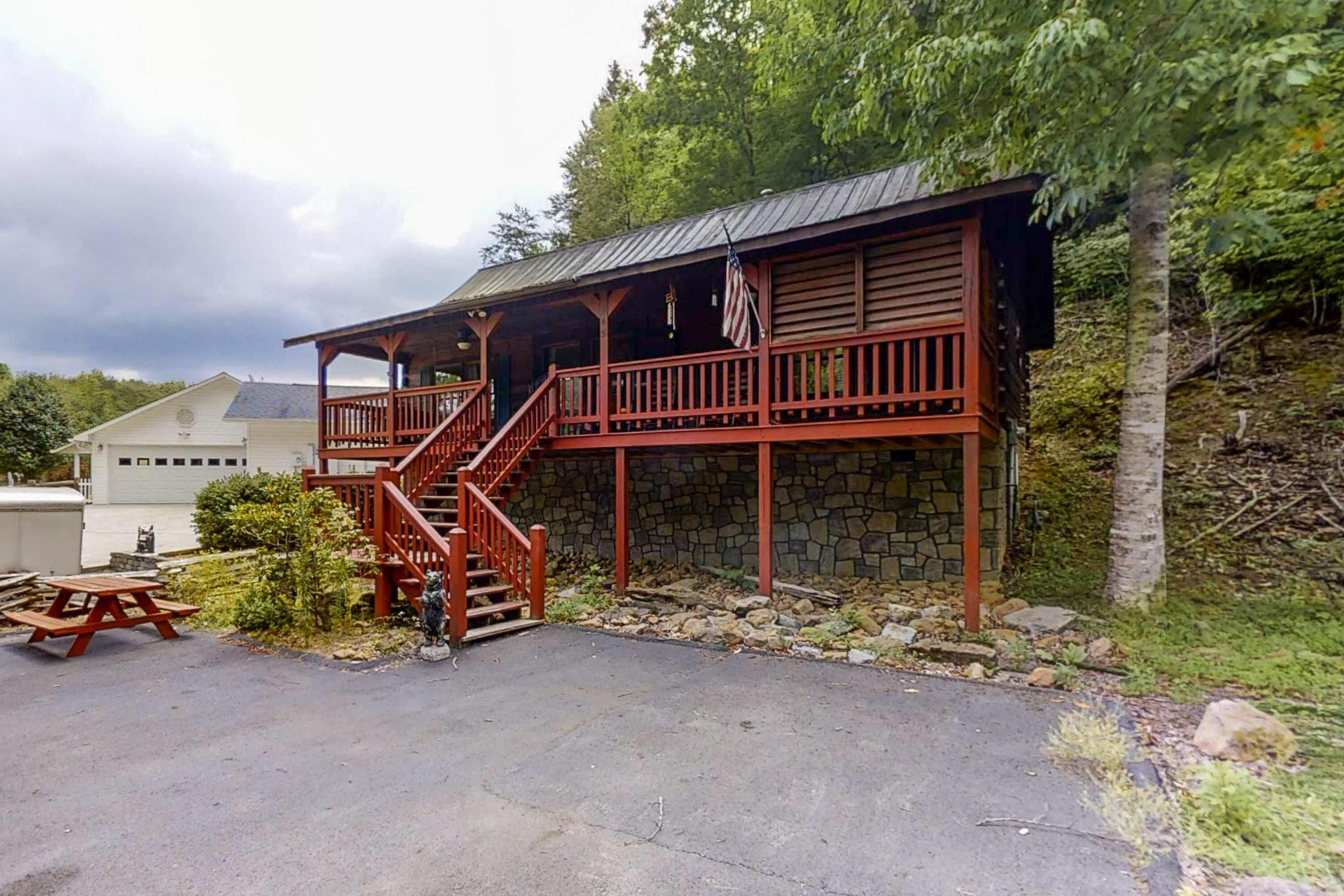 Une cabane rustique avec des fondations en pierre, une terrasse en bois et un escalier menant à un porche abrité.