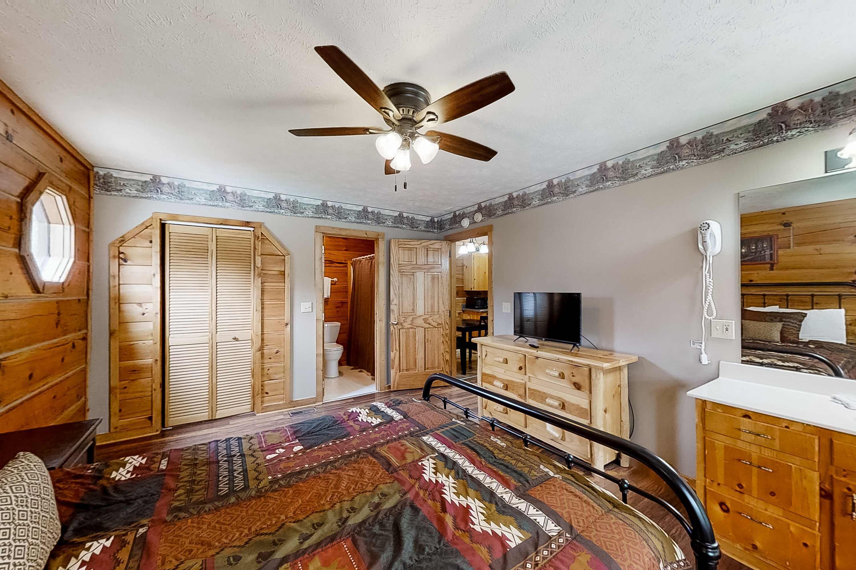 Une chambre à coucher avec un lit, une armoire en bois, une télévision et un ventilateur de plafond.