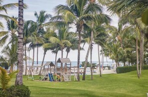 A beach area with palm trees, a playground, and a view of the ocean. - Seawinds Beachfront Top Floor- Less Mosquitos•24/7 Security (Sousa-Cabarete Highway)