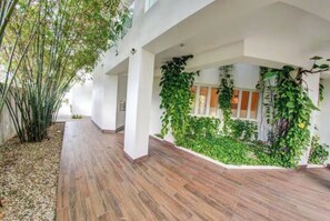 A covered walkway with wooden flooring, white walls, and green plants growing along the edges. - Seawinds Beachfront Top Floor- Less Mosquitos•24/7 Security (Sousa-Cabarete Highway)