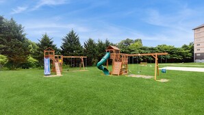 Ein Spielplatz mit zwei hölzernen Spielgeräten, darunter Rutschen und Schaukeln, auf einer grünen Rasenfläche.