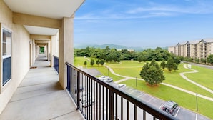 Ein Balkon mit Blick auf einen grünen Park, einen Parkplatz und entfernte Gebäude.