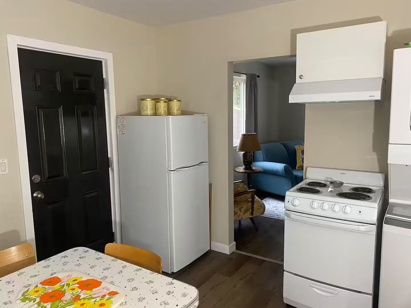 Een kleine keuken met een koelkast, fornuis en een eethoek met een tafel en stoelen.