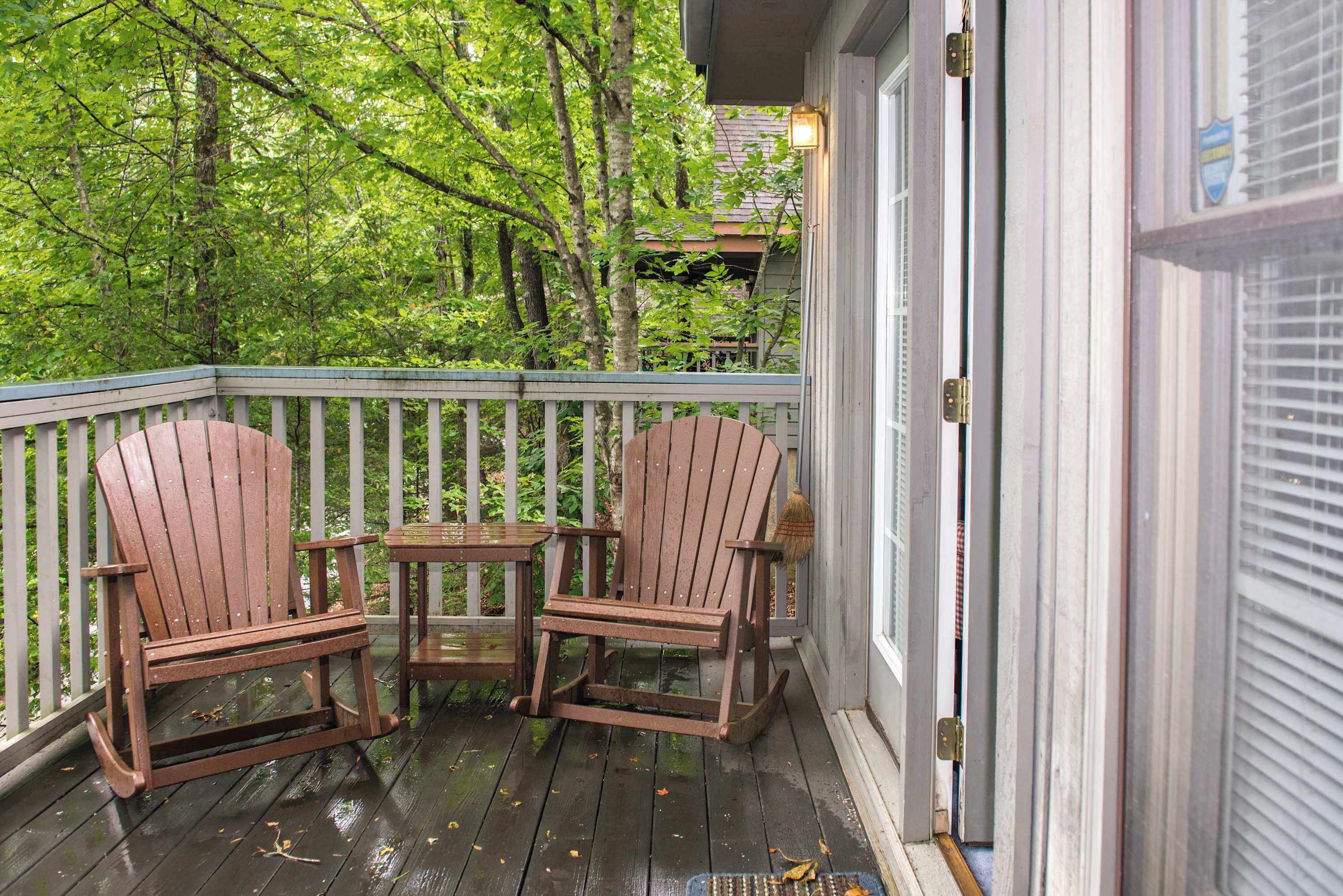 A wooden deck with two Adirondack chairs and a small table, surrounded by a white railing.