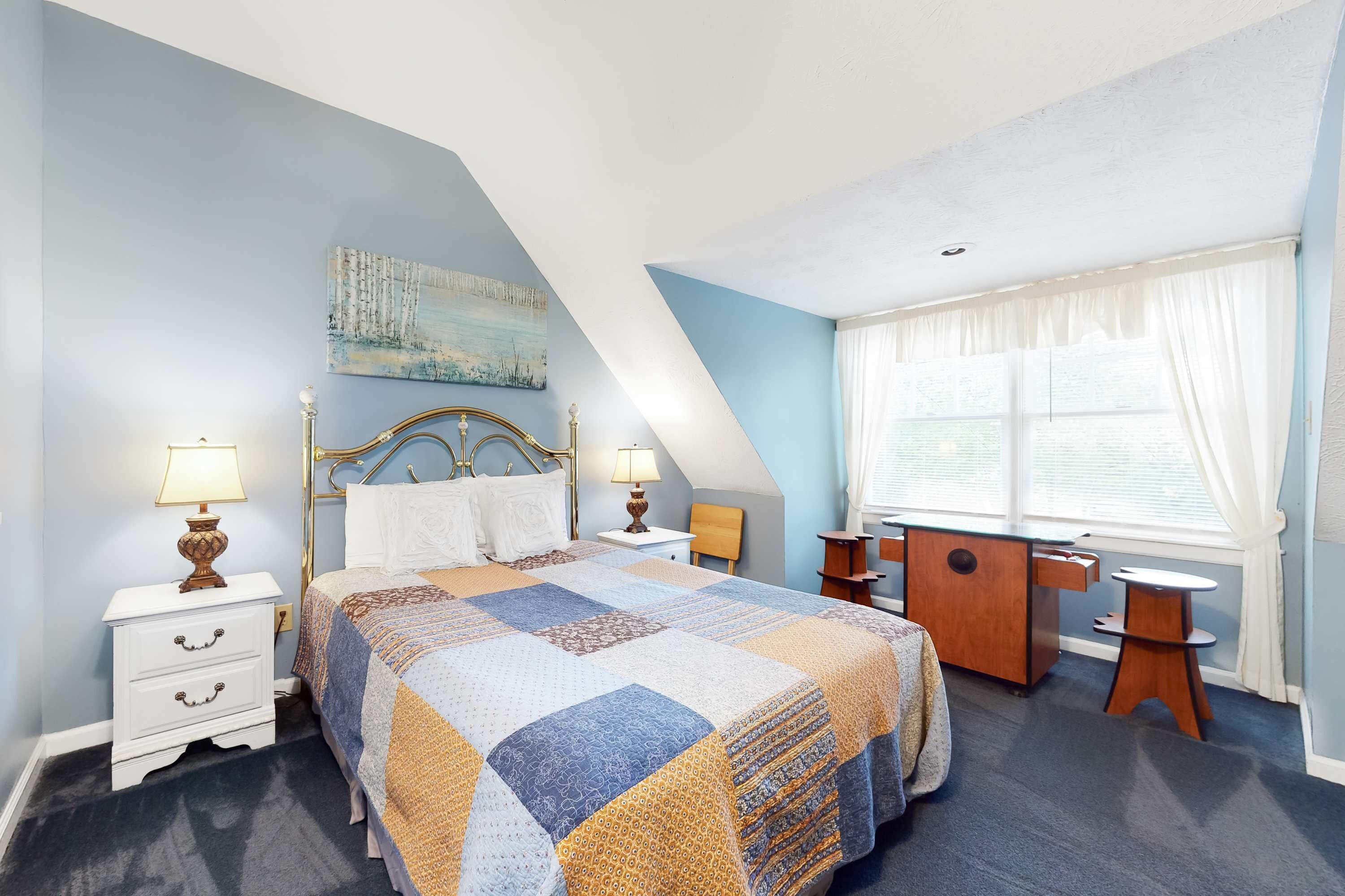 A bedroom with a bed, two bedside tables, a desk, and a window with curtains.