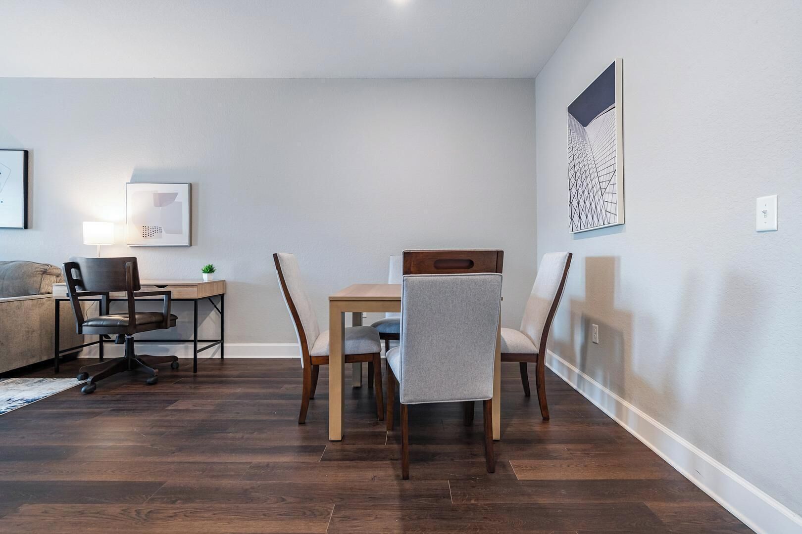 Un salon moderne comprenant une table à manger, quatre chaises, un canapé et un bureau avec une lampe.