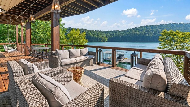 A covered outdoor seating area with wicker furniture and a view of a lake.