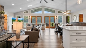 A spacious living area with a high ceiling, large windows, and a kitchen with a white countertop.