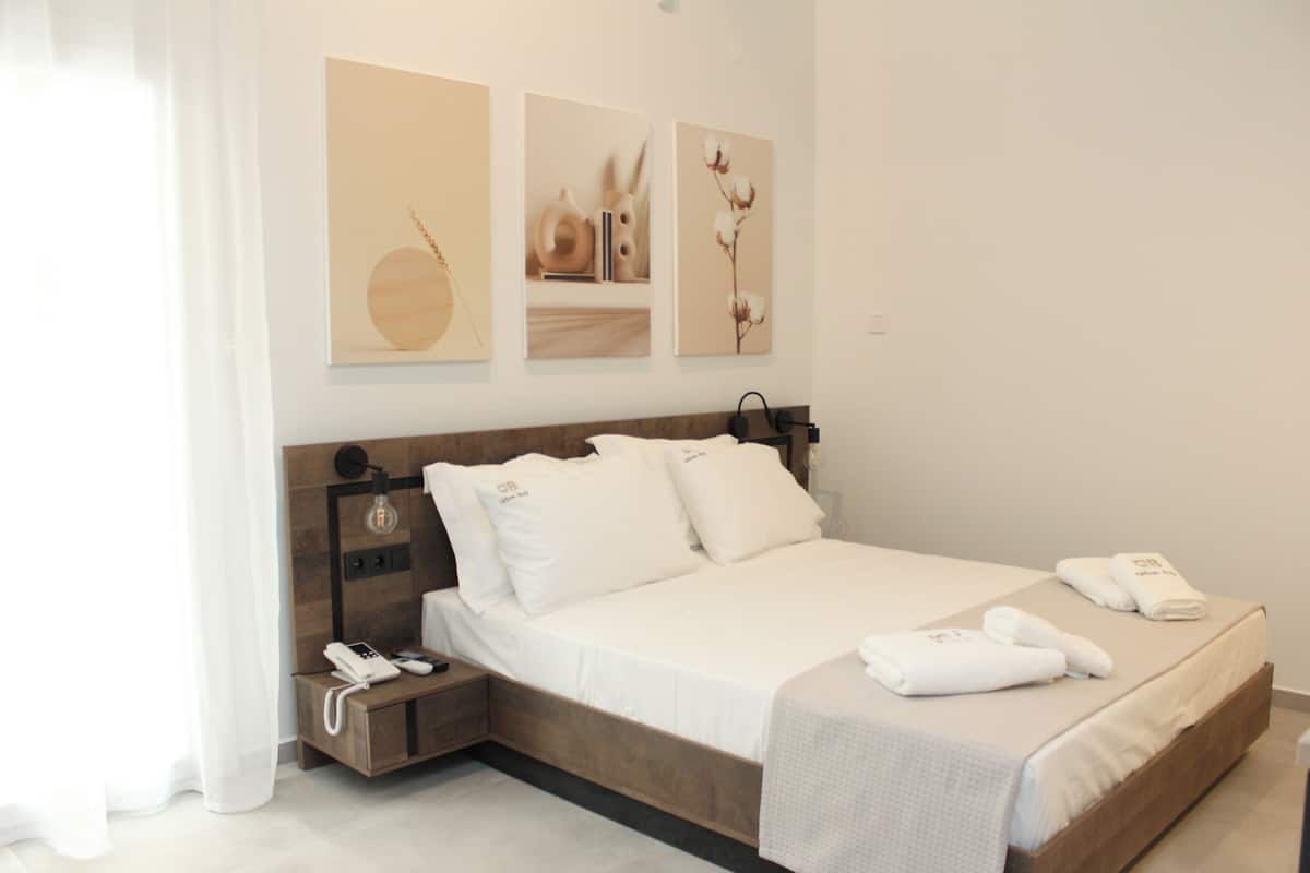 A neatly made bed with white linens and pillows, a bedside table with a phone and a lamp, and artwork on the wall.