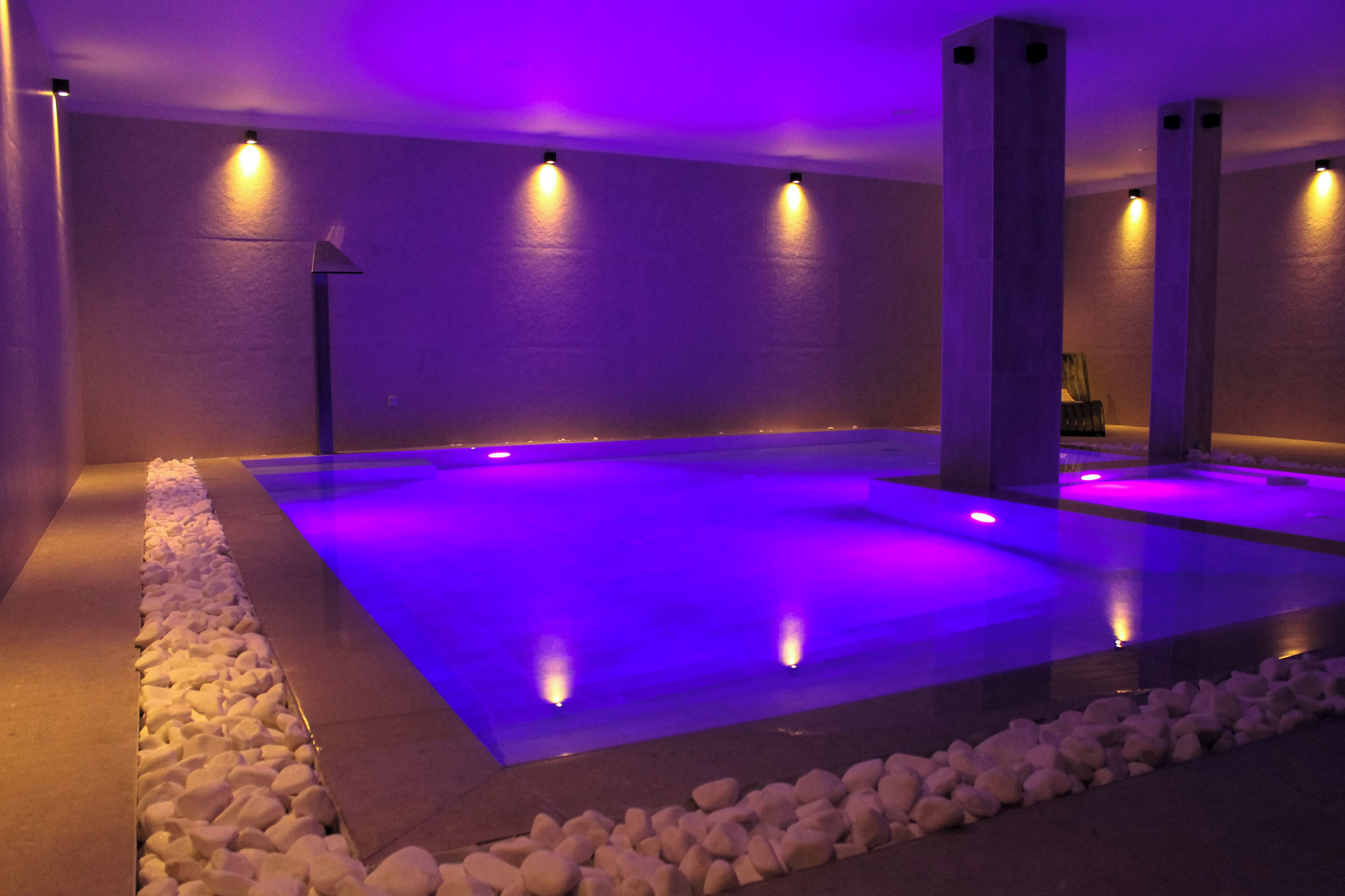 A spa area with a rectangular pool, stone seating, and ambient lighting.