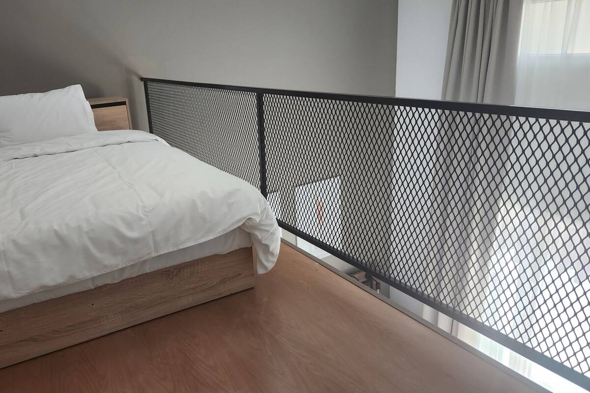 A bedroom with a wooden bed, white bedding, a black mesh headboard, and a view of the outdoors.