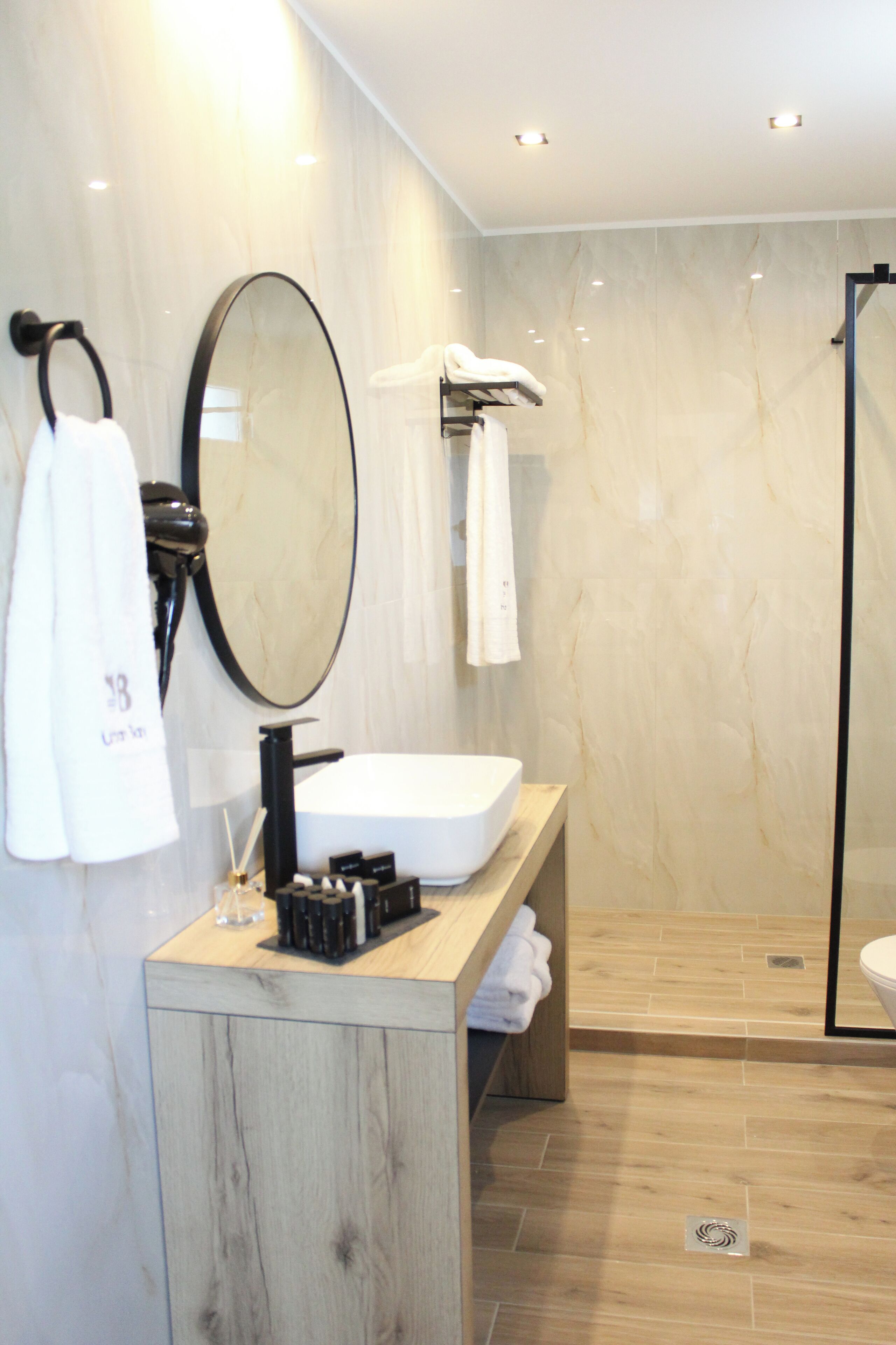 A modern bathroom with a wooden vanity, a large mirror, and a glass shower enclosure.