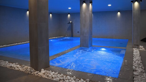 Zona de spa con dos jacuzzis, pilares de piedra y una fuente de agua.