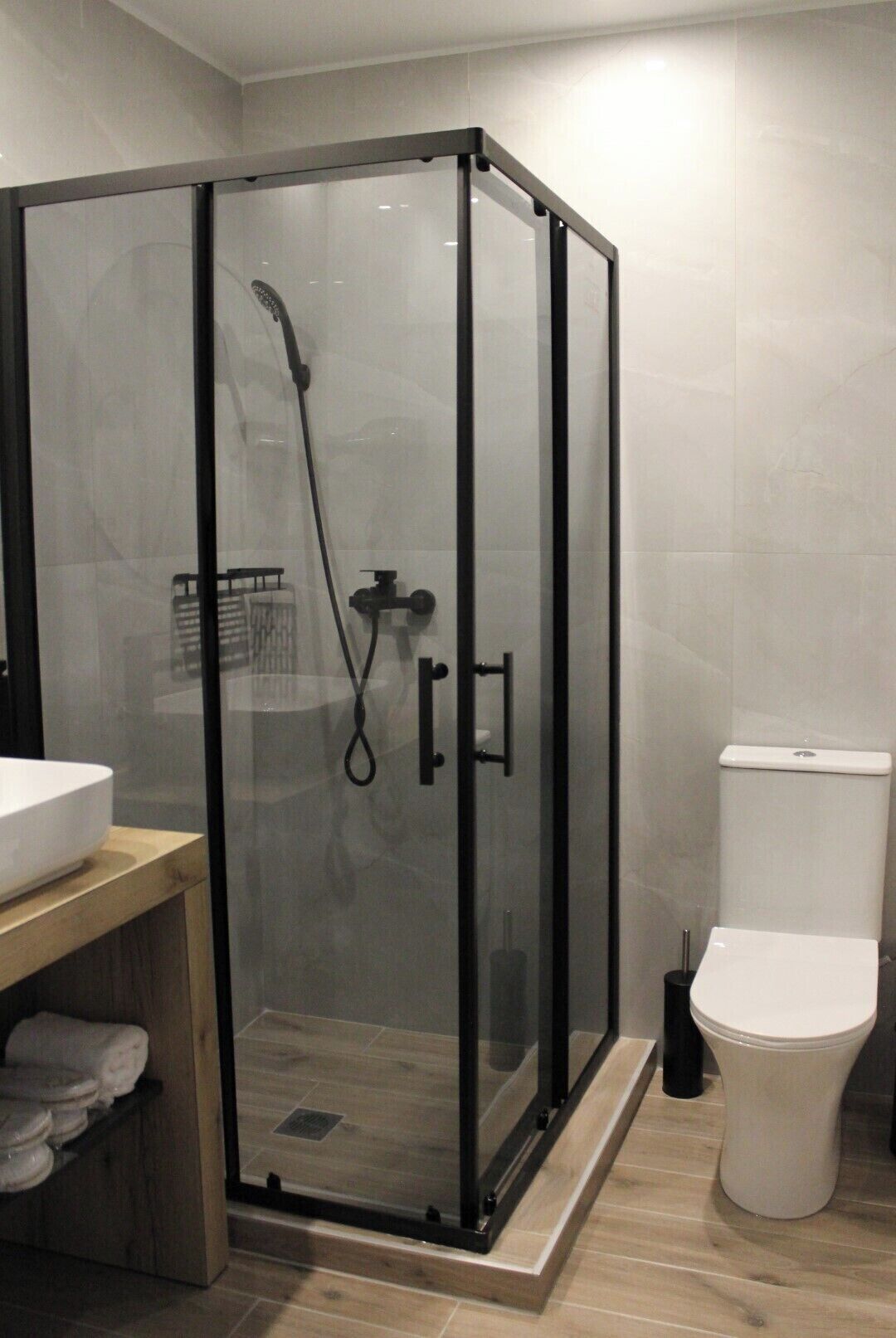 A modern bathroom with a glass-enclosed shower, a white toilet, and a wooden vanity with a sink.