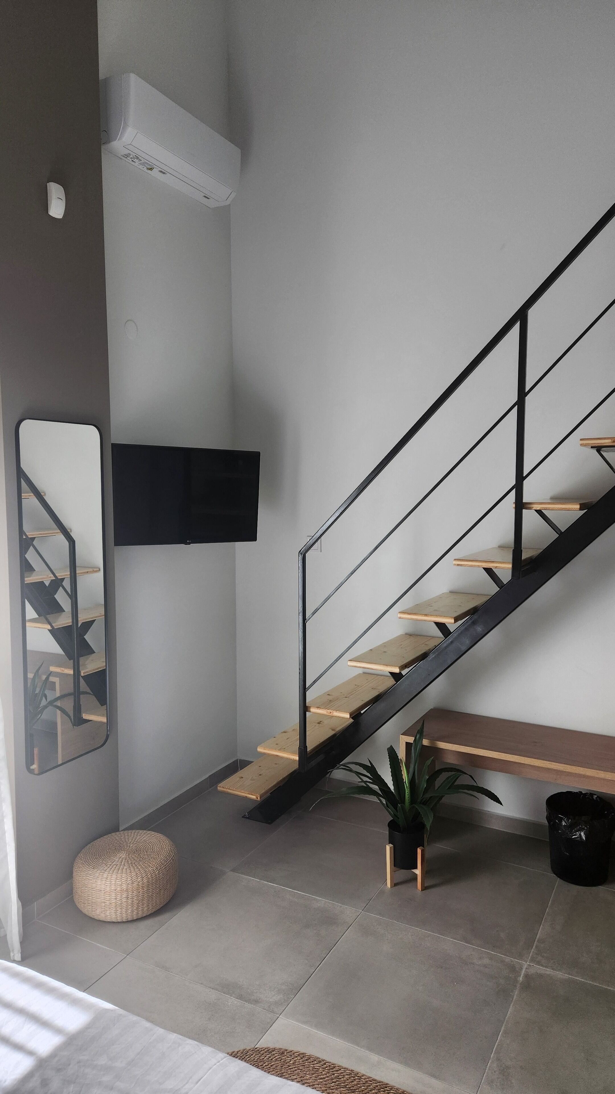 A modern interior with a staircase, a mounted TV, a potted plant, and a woven ottoman.