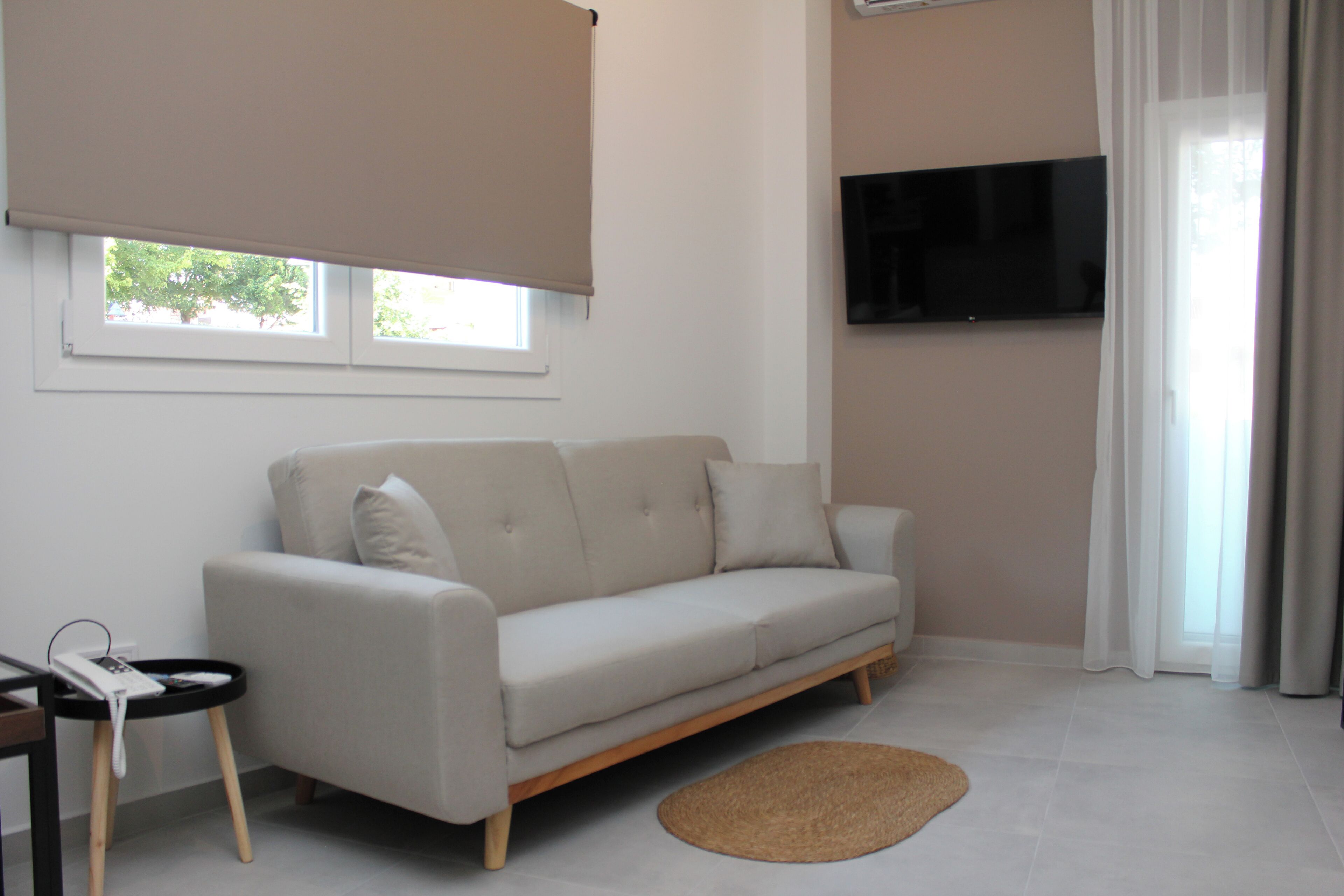 A modern living room with a sofa, a flat-screen TV, and a window with blinds.