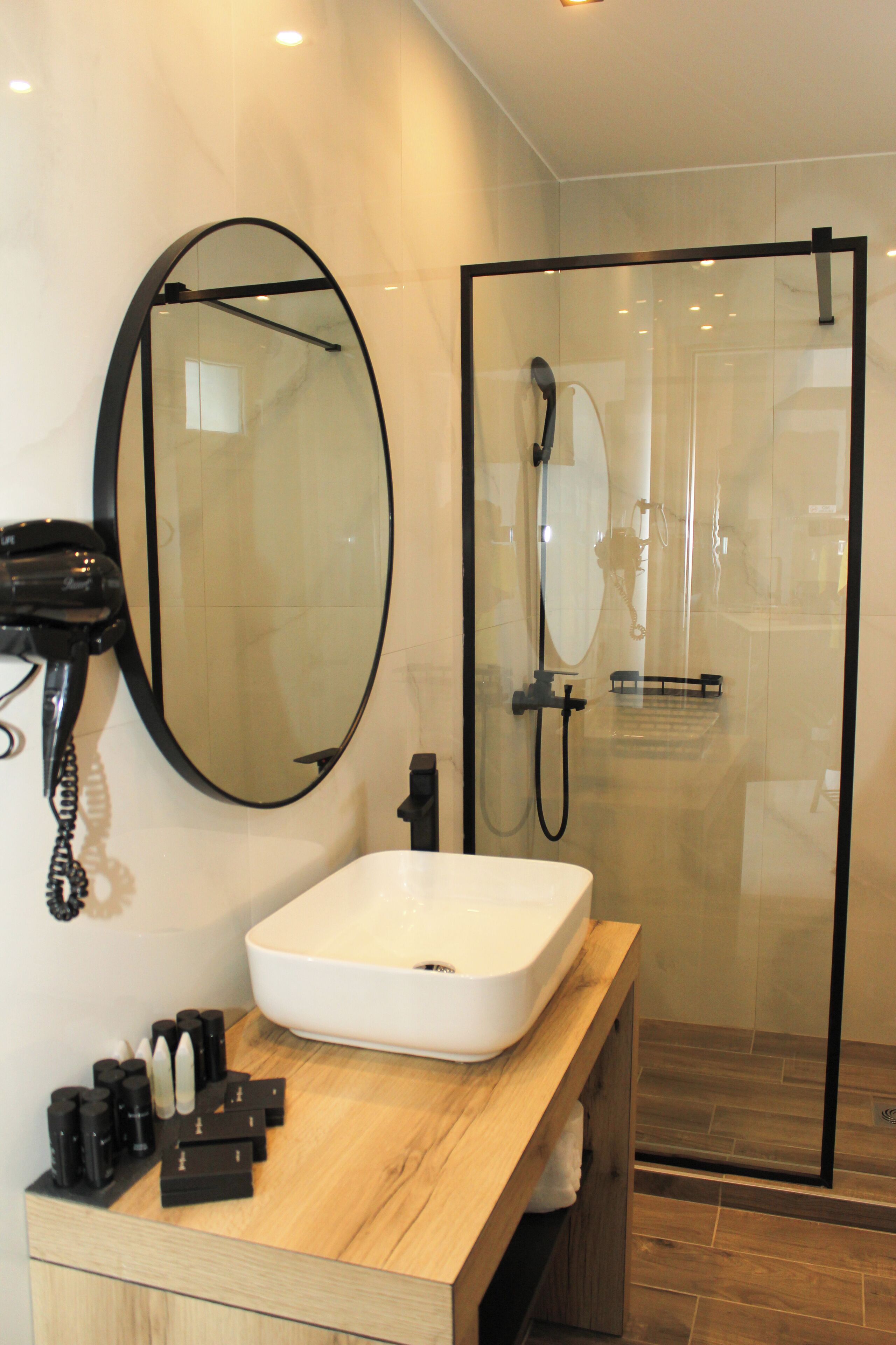A modern bathroom with a large oval mirror, a white sink, and a glass-enclosed shower.
