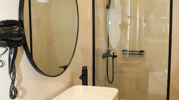 A modern bathroom with a large oval mirror, a white sink, and a glass-enclosed shower.