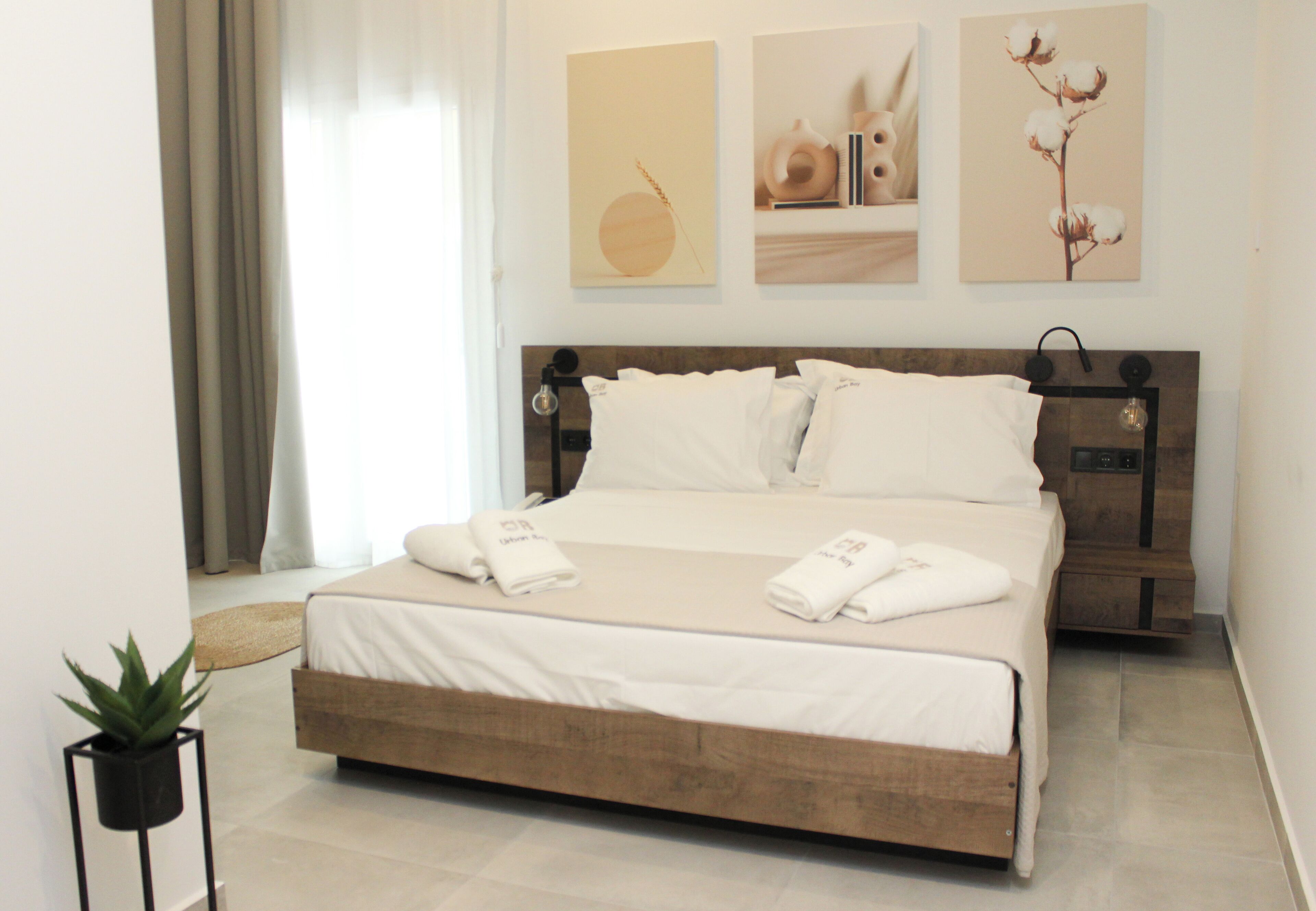 Una cama bien hecha con ropa y toallas blancas, una mesita de noche con lámpara y una obra de arte en la pared.