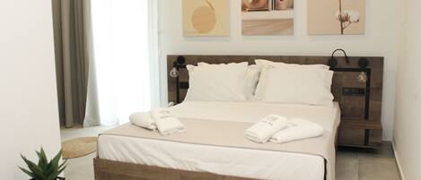 Una cama bien hecha con ropa y toallas blancas, una mesita de noche con lámpara y una obra de arte en la pared.
