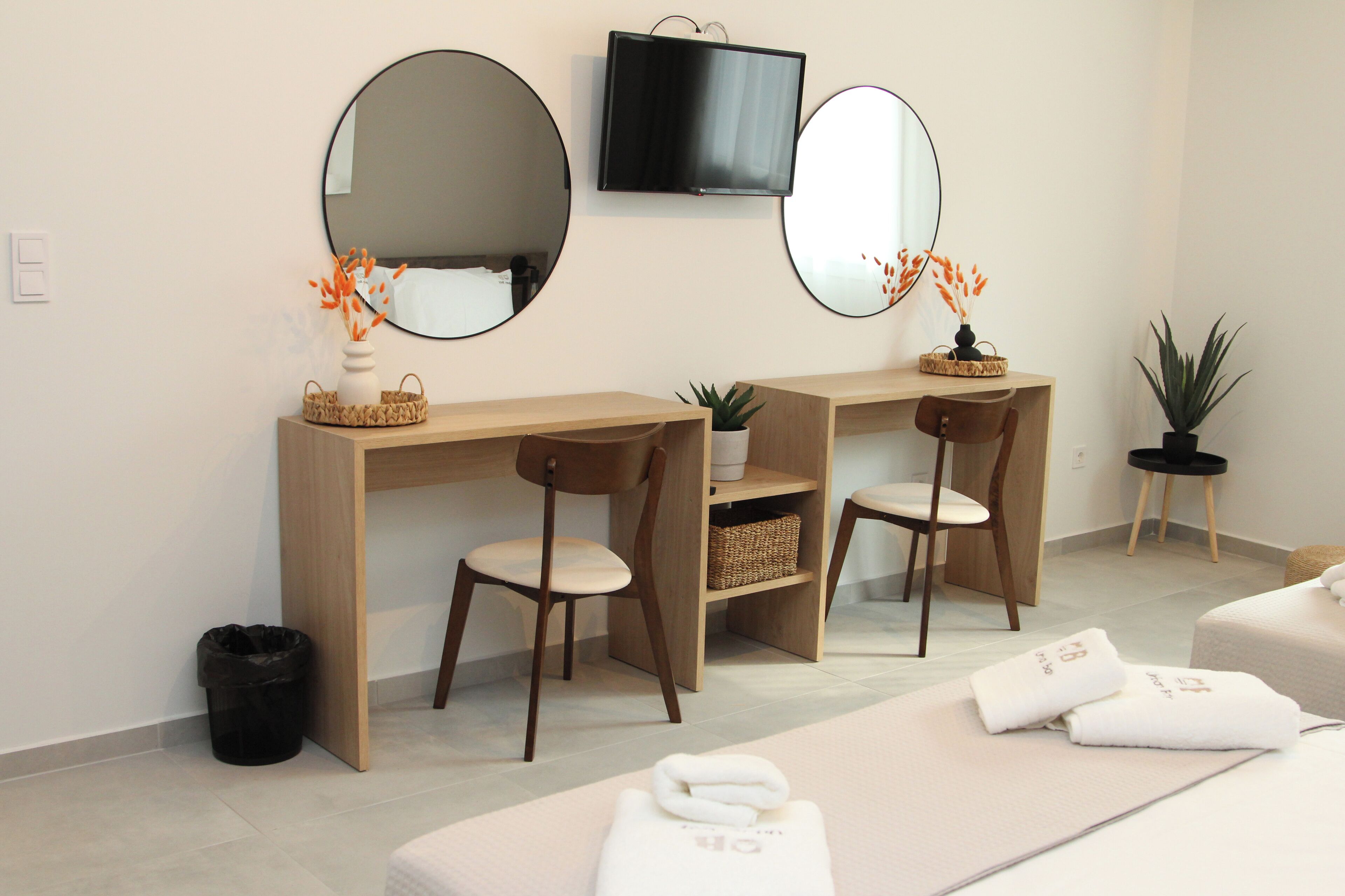 A modern room with a wooden desk, two chairs, a TV, and a massage table with towels.
