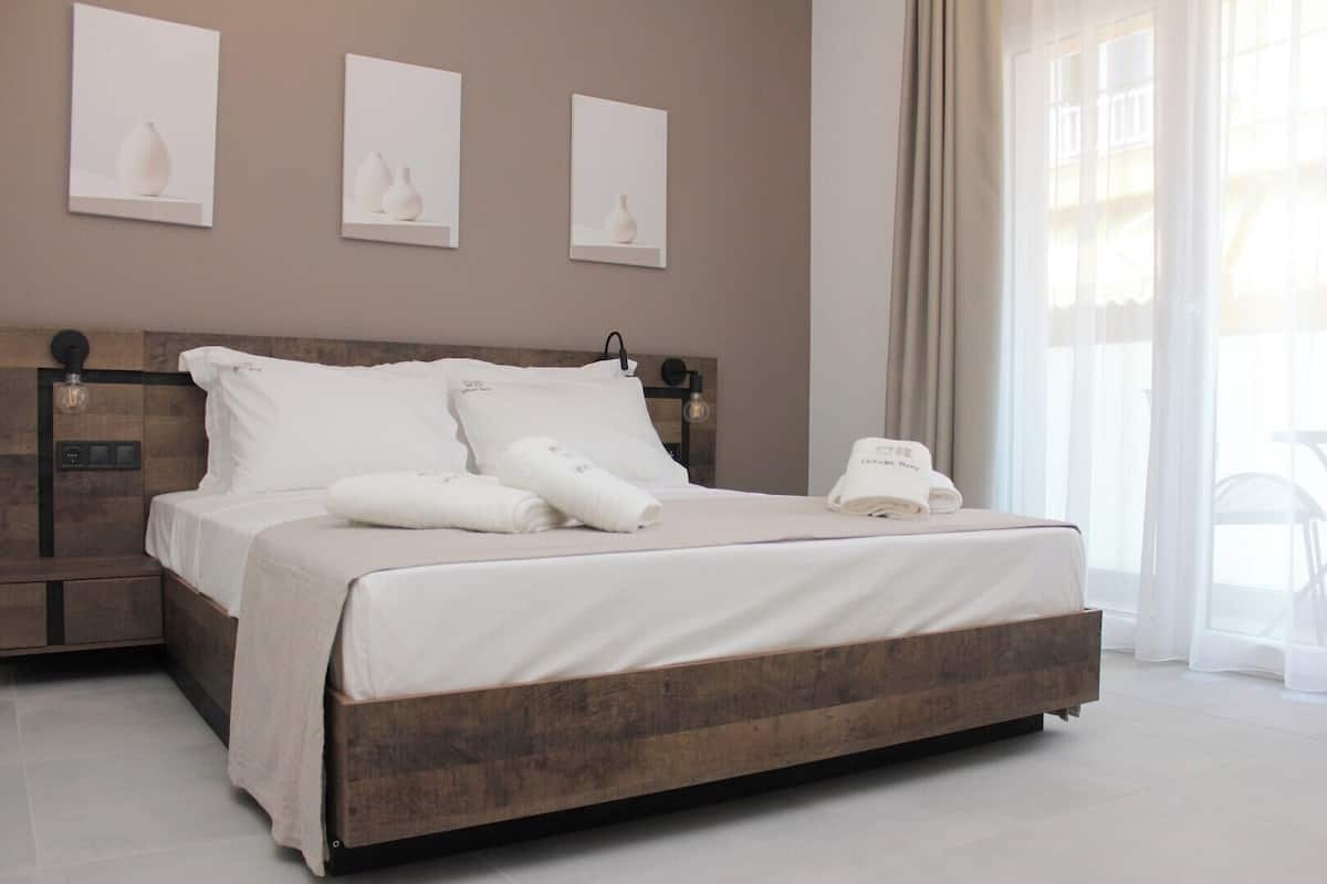 A neatly made bed with white linens and towels, a wooden headboard, and three framed artworks on the wall.